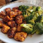 A serving of glazed chicken pieces next to bright green roasted chicken and broccoli.