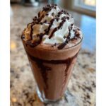 A tall glass of rich, blended frozen hot chocolate topped with whipped cream, chocolate syrup, and mini chocolate chips.