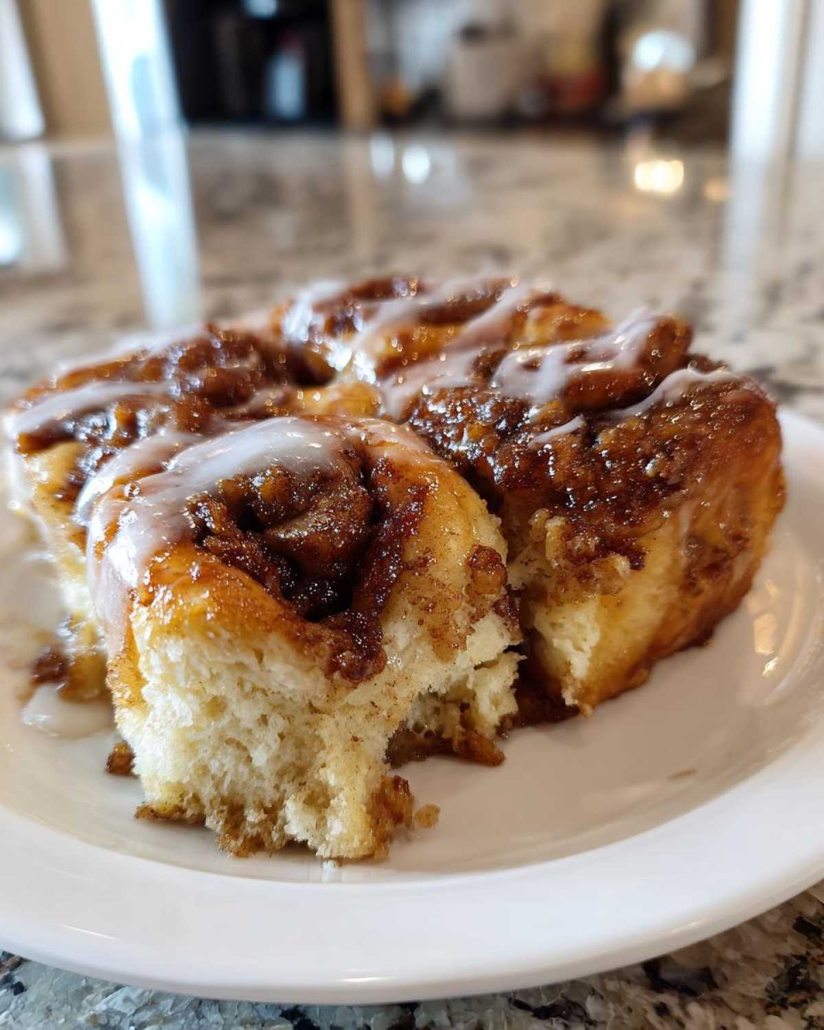 A close-up of a serving of gooey, glazed Cinnamon roll casserole on a white plate.
