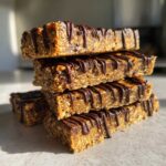 A stack of four homemade protein bars drizzled with melted dark chocolate, showing texture.