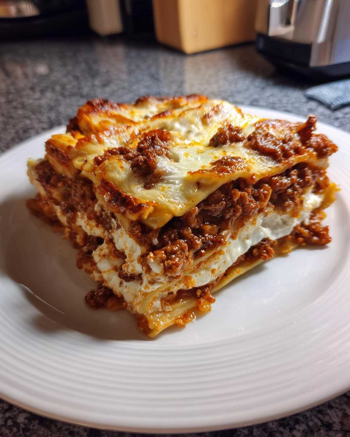 A thick, perfectly layered slice of amazing 3 layer lasagna featuring rich meat sauce and creamy white cheese filling.