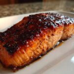 Close-up of a perfectly baked salmon fillet with a dark, caramelized glaze resting on a white plate.