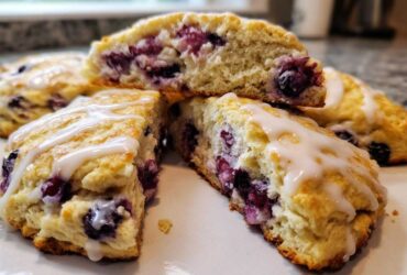 Close-up of fluffy blueberry scones, cut open to show the fruit filling and drizzled with white glaze.