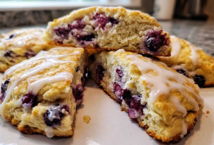 Close-up of fluffy blueberry scones, cut open to show the fruit filling and drizzled with white glaze.