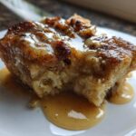 Close-up of a rich, baked slice of bread pudding topped with a creamy caramel sauce.