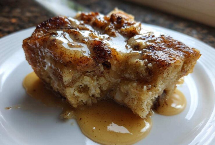 Close-up of a rich, baked slice of bread pudding topped with a creamy caramel sauce.