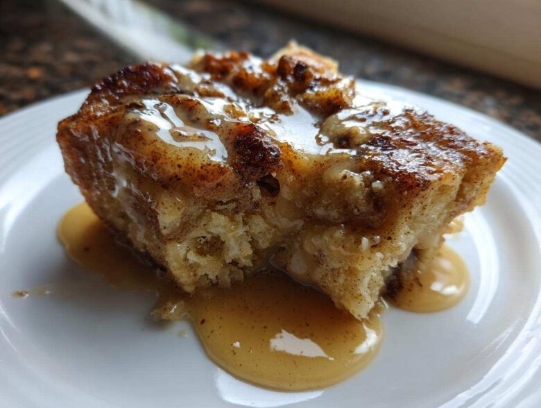 Close-up of a rich, baked slice of bread pudding topped with a creamy caramel sauce.