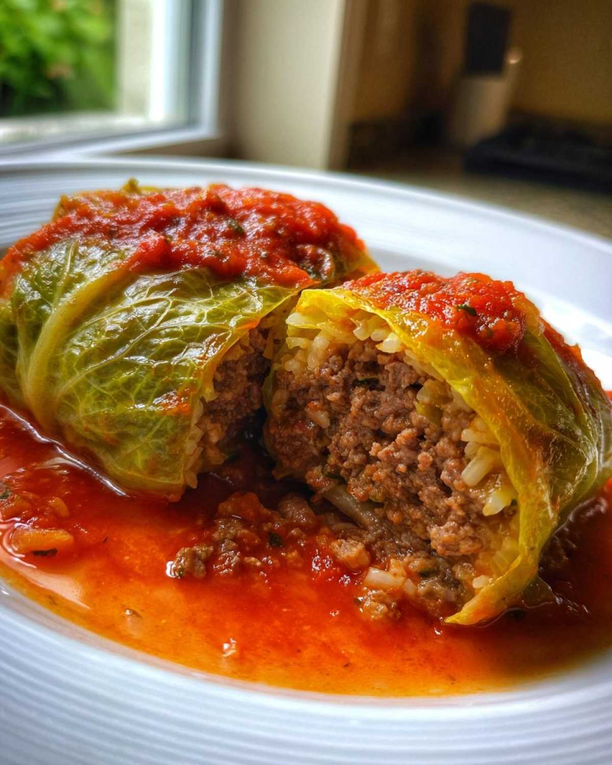 Close-up of two delicious cabbage rolls cut open, showing the ground meat and rice filling, served in a vibrant tomato sauce.