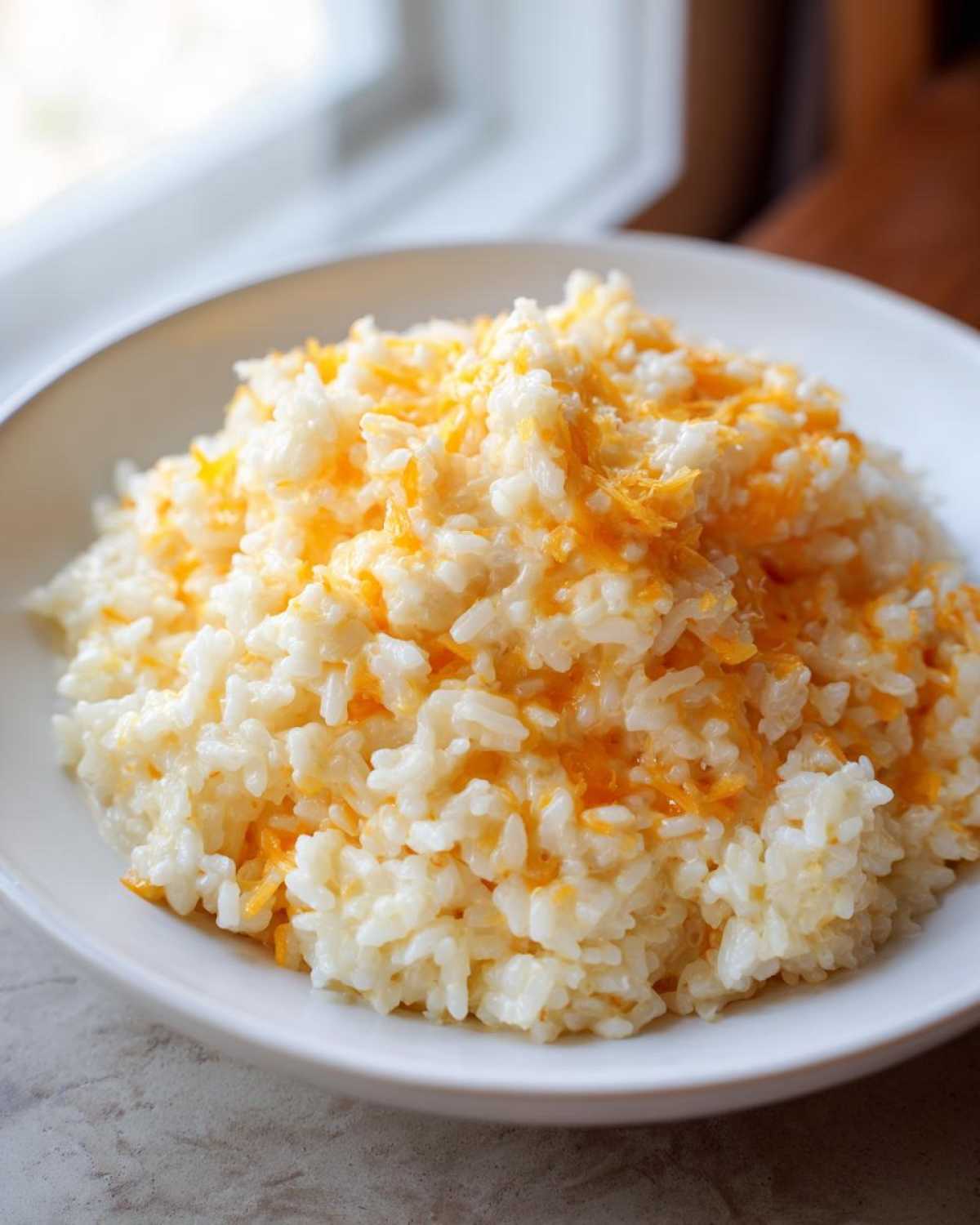 A white bowl filled with creamy, fluffy cheesy rice topped with melted orange cheddar cheese.