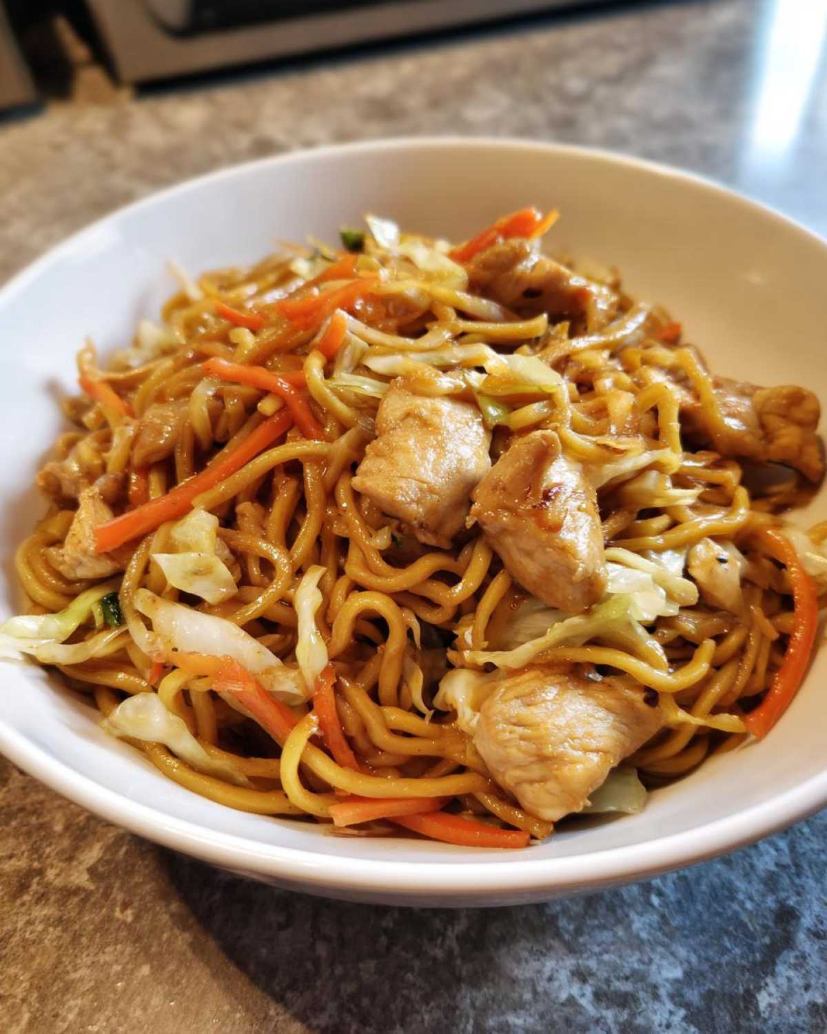 A close-up bowl filled with delicious chicken chow mein recipe, featuring noodles, chicken pieces, and shredded carrots and cabbage.