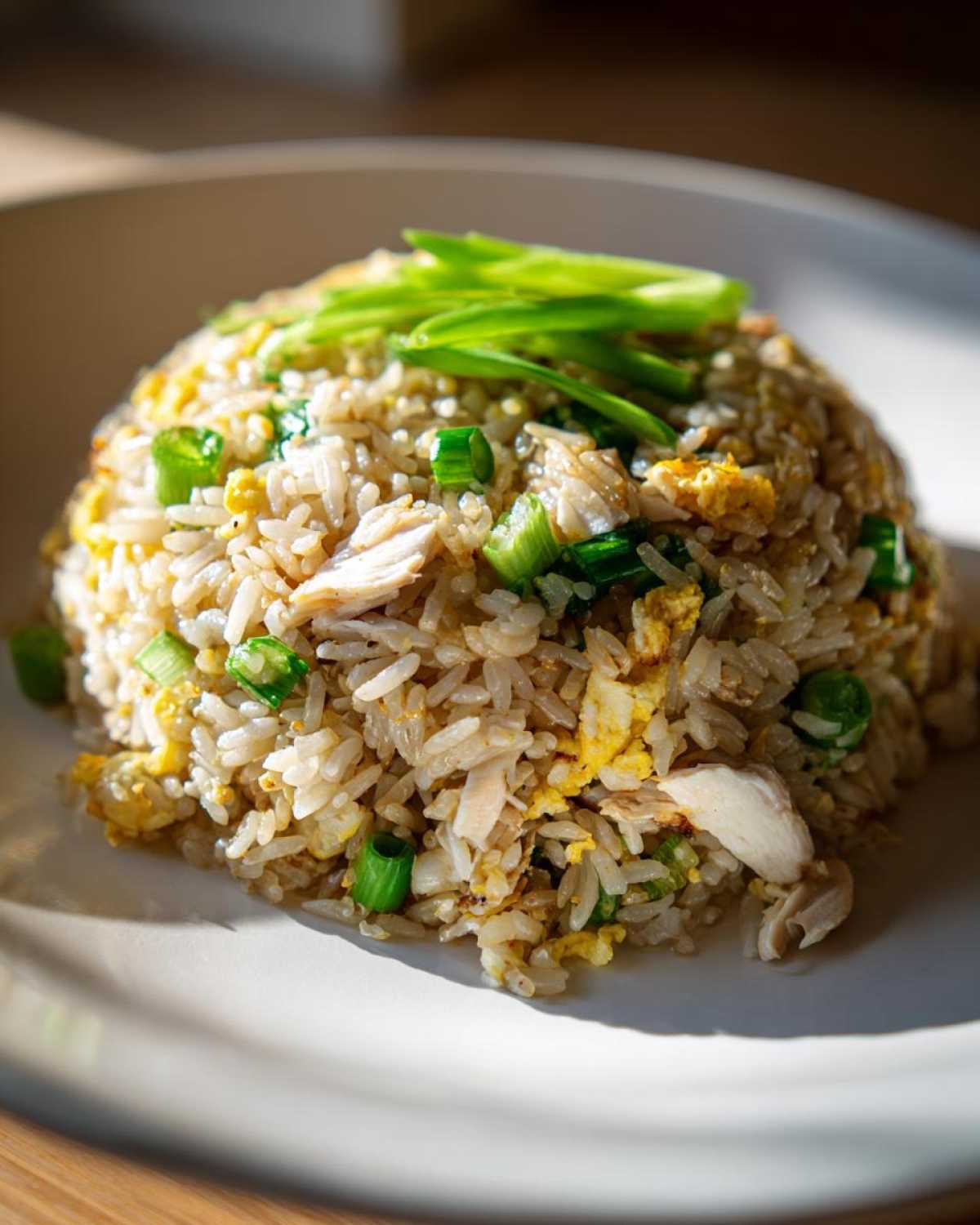 A perfectly mounded serving of homemade chicken fried rice, featuring visible pieces of chicken, scrambled egg, and green onions.