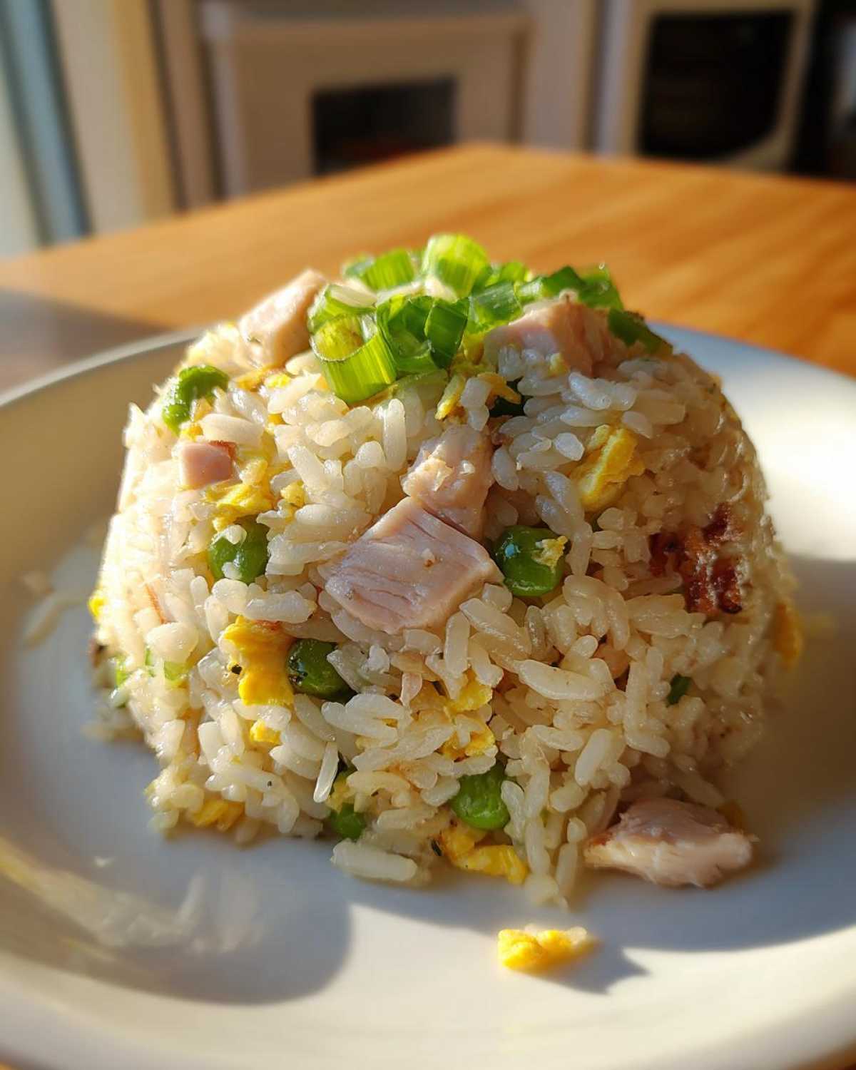 A mound of homemade chicken fried rice featuring chunks of chicken, peas, and egg, topped with fresh green onions.