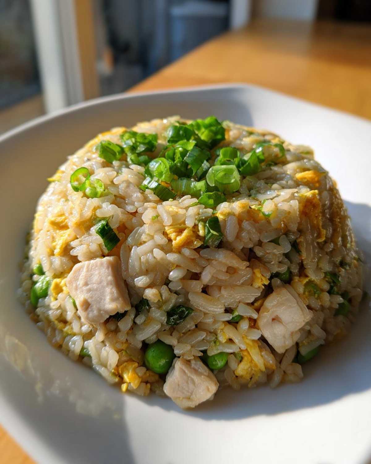 A mound of homemade chicken fried rice featuring white rice, scrambled egg, chicken cubes, and peas, topped with fresh green onions.