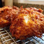 Close-up of two pieces of golden brown, extra-crispy fried chicken resting on a wire cooling rack.