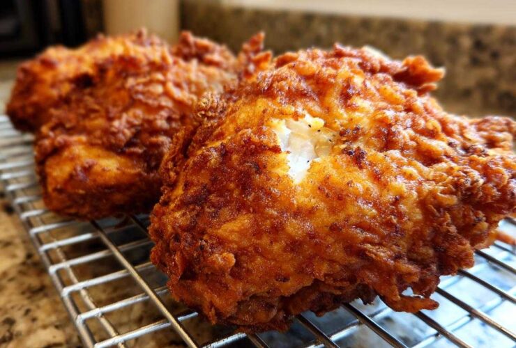 Close-up of two pieces of golden brown, extra-crispy fried chicken resting on a wire cooling rack.
