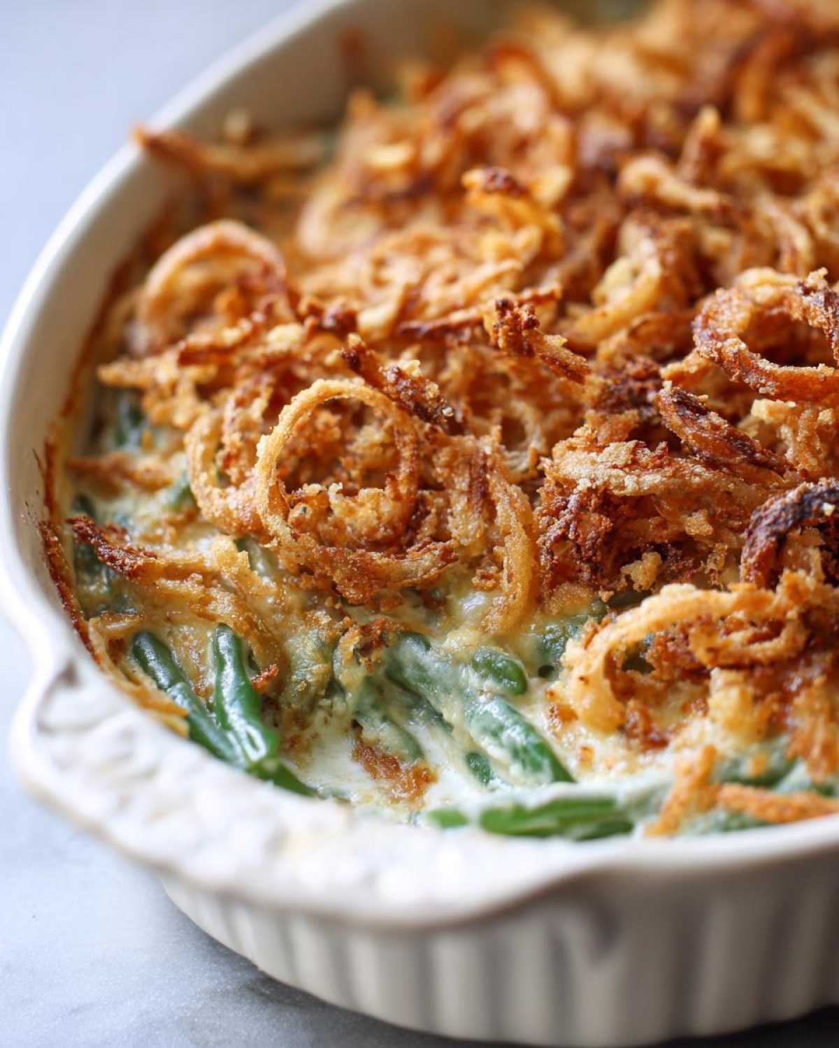 A close-up shot of a creamy green bean casserole topped generously with golden, crispy fried onions.
