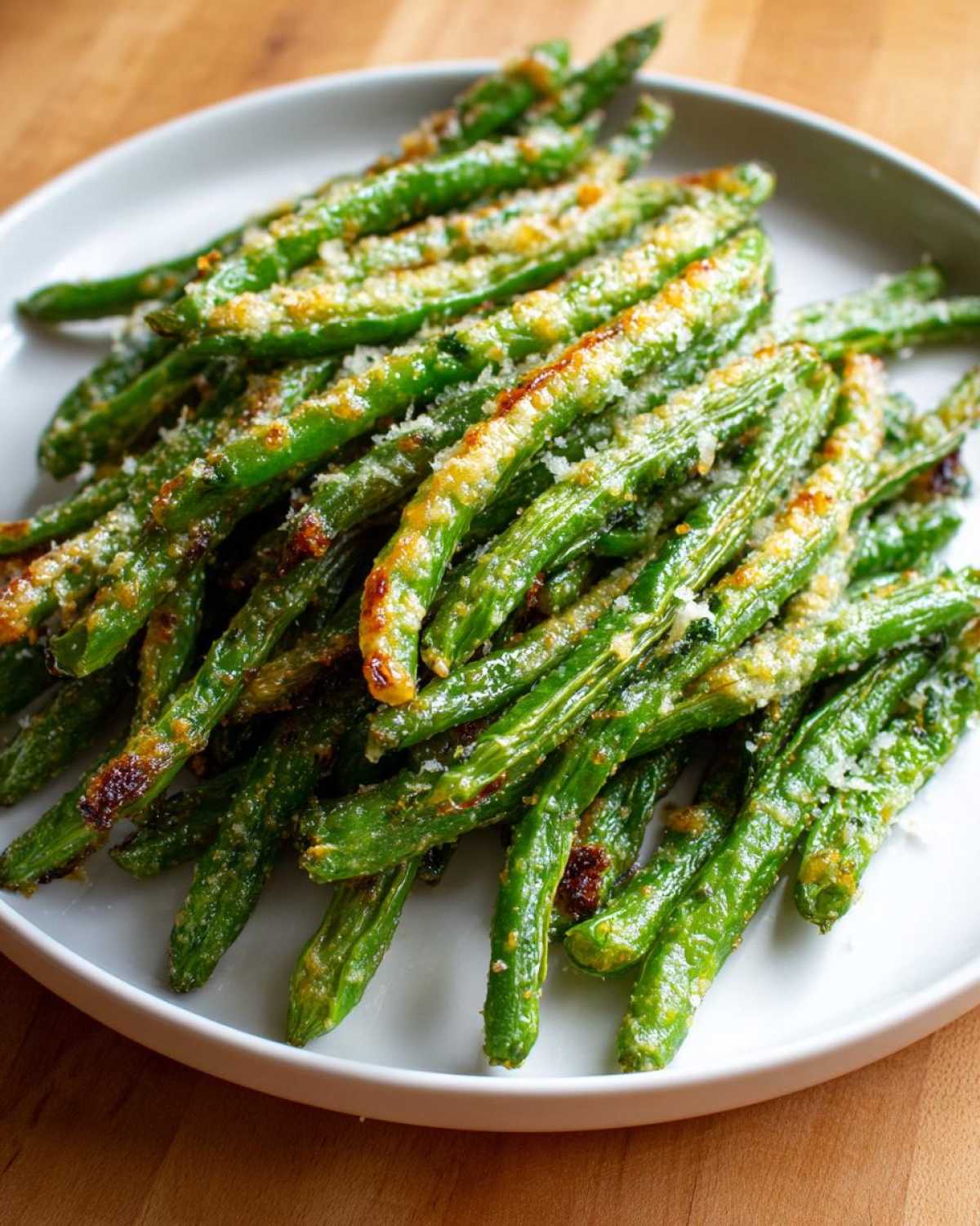 A pile of bright green beans roasted with parmesan cheese served on a white plate.