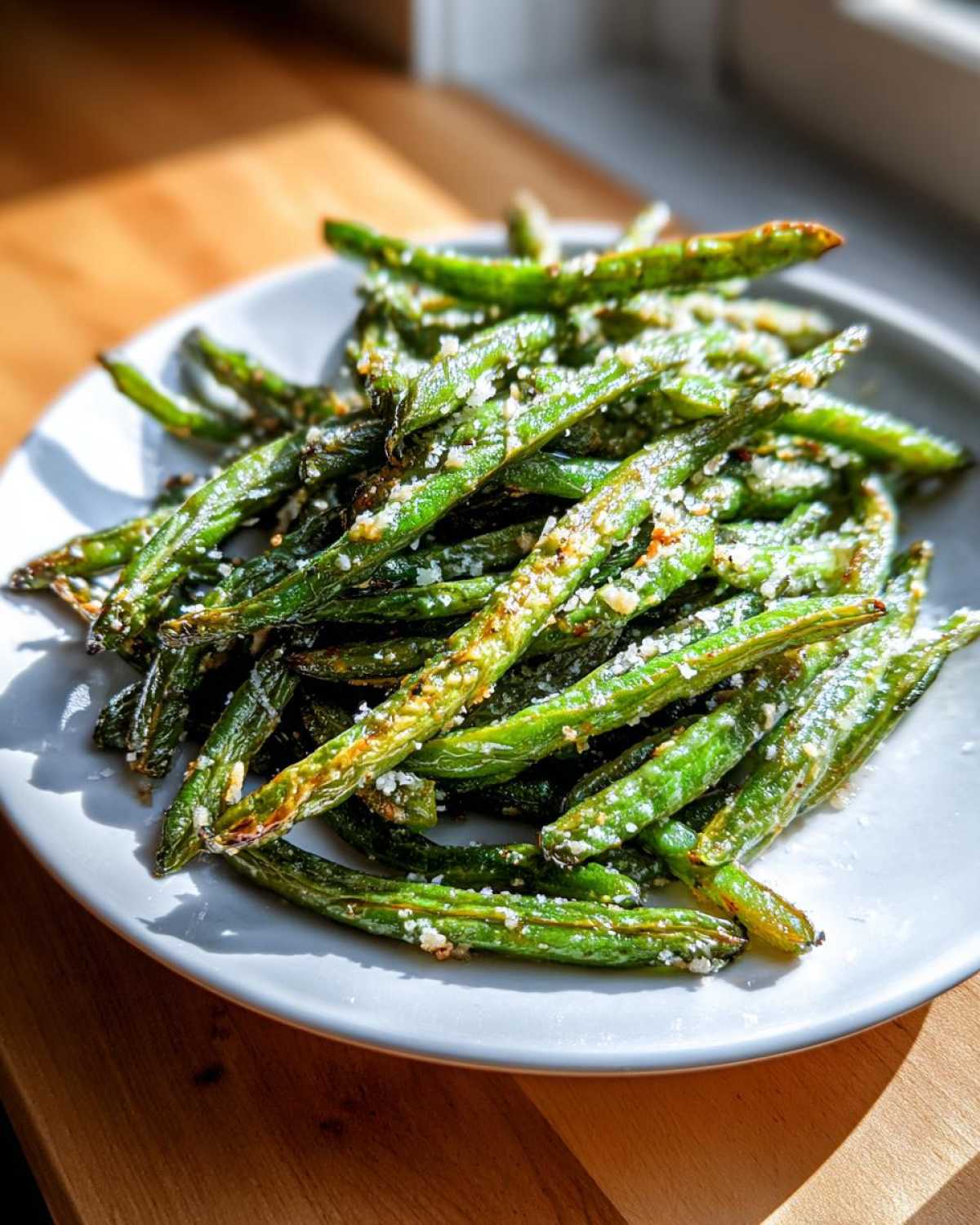 A close-up of roasted green beans sprinkled with grated cheese on a white plate.