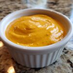 Close-up of creamy, bright orange homemade nacho cheese served in a small white ramekin.