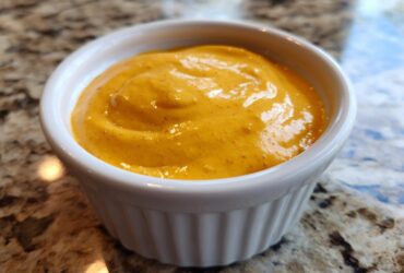 Close-up of creamy, bright orange homemade nacho cheese served in a small white ramekin.