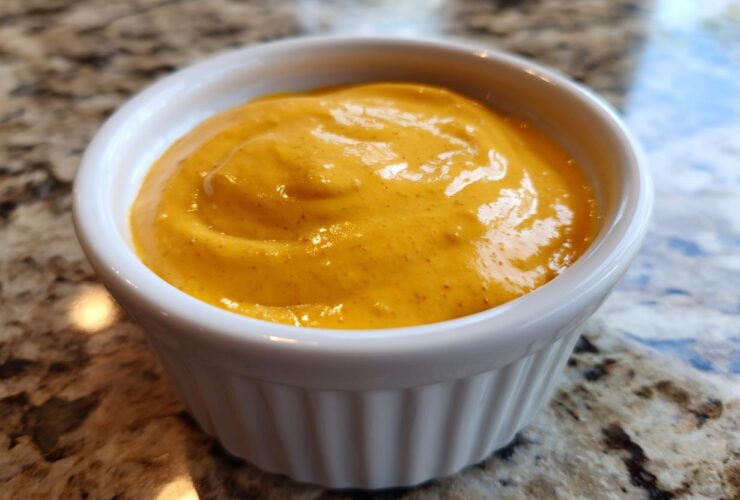 Close-up of creamy, bright orange homemade nacho cheese served in a small white ramekin.