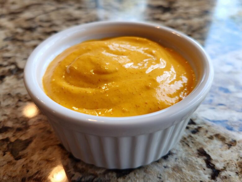 Close-up of creamy, bright orange homemade nacho cheese served in a small white ramekin.