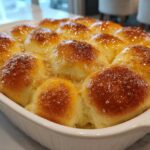 Close-up of freshly baked, soft dinner rolls glistening with a sweet, buttery glaze in a white baking dish.