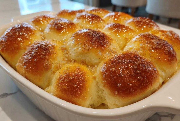 Close-up of freshly baked, soft dinner rolls glistening with a sweet, buttery glaze in a white baking dish.