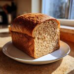 A freshly baked loaf of whole wheat bread, sliced to show the soft interior crumb, sitting on a white plate.