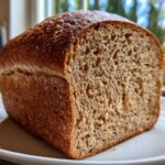 A close-up of a freshly baked loaf of whole wheat bread, showing its dark crust and open crumb structure.
