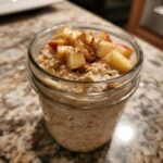 Close-up of apple cinnamon overnight oats in a glass jar, topped with fresh diced apples and cinnamon.