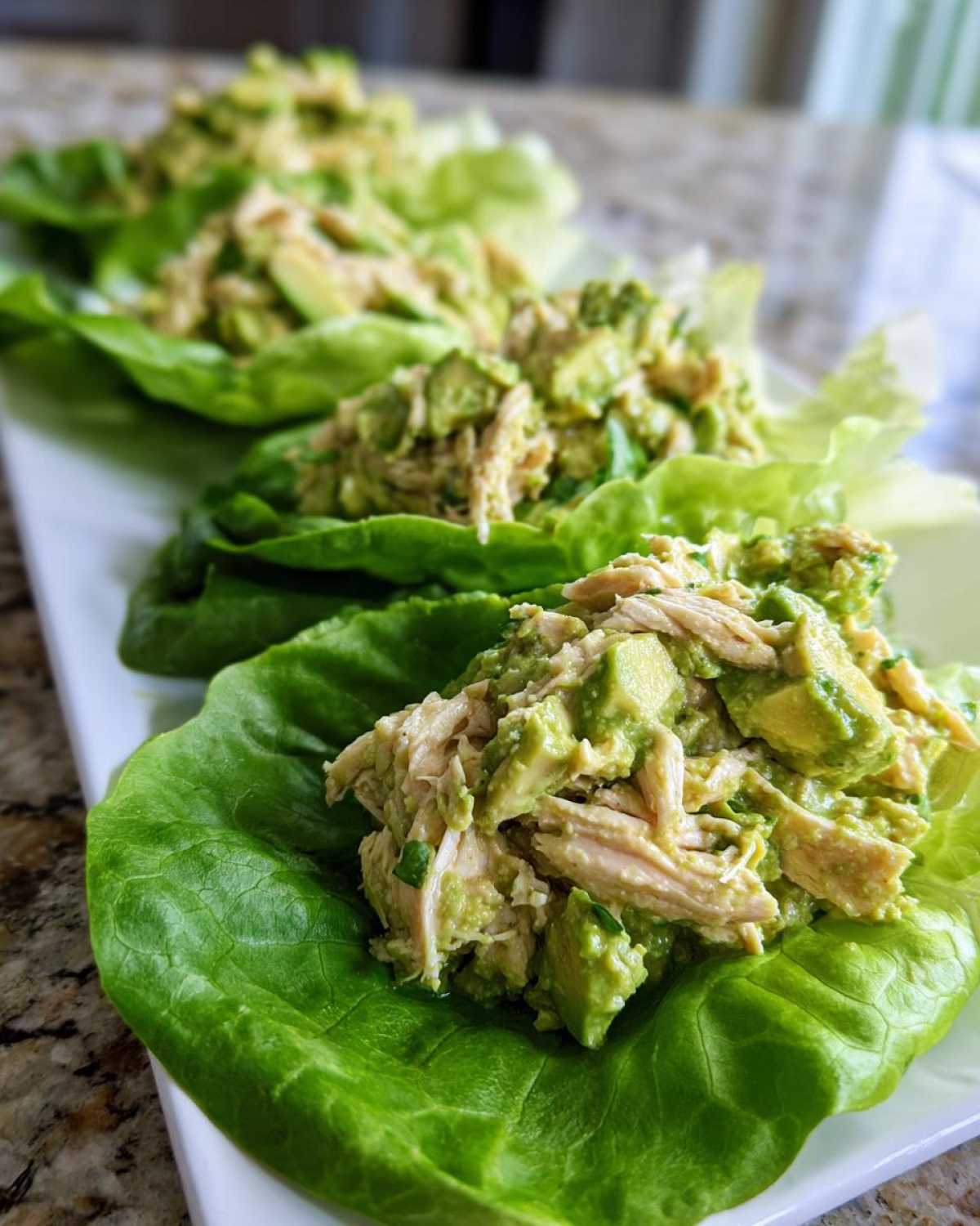 Close-up of shredded chicken mixed with chunks of avocado, served as avocado chicken salad in crisp lettuce cups.