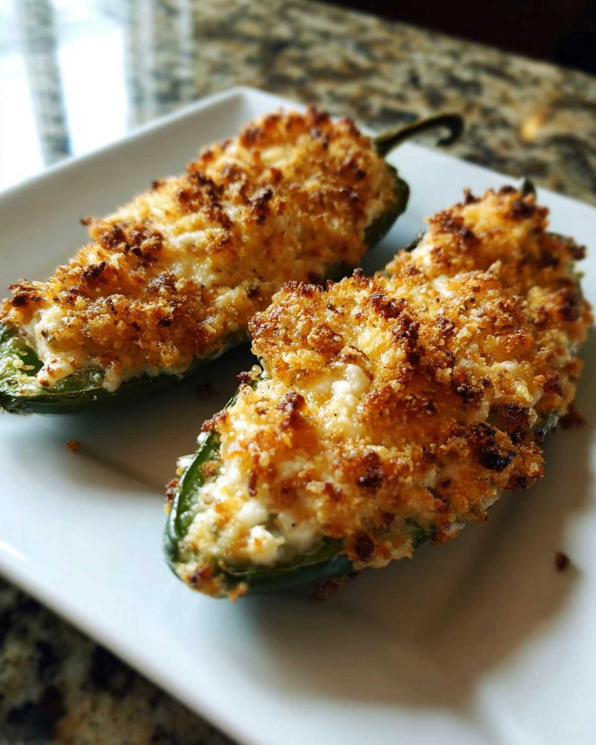 Two baked Jalapeño poppers stuffed with creamy filling and topped with golden brown crispy breadcrumbs.