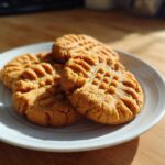 A stack of freshly baked peanut butter cookies with classic criss-cross fork marks resting on a white plate.
