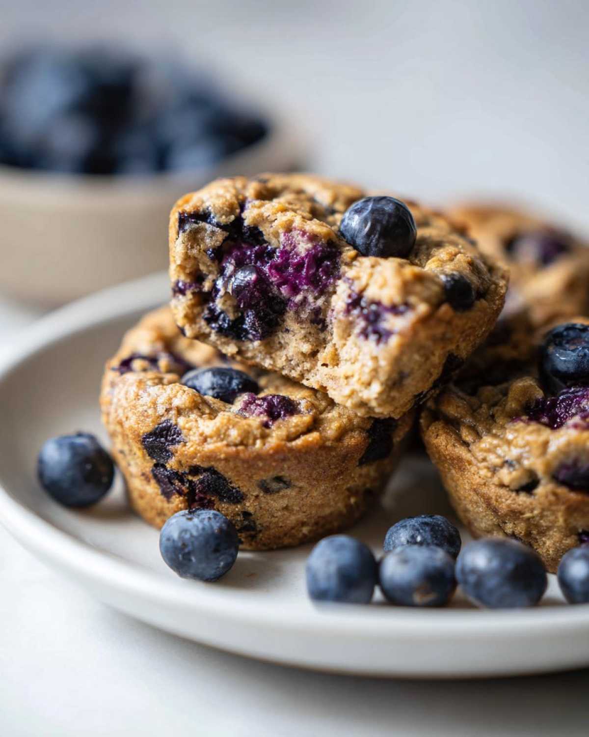 Close-up of delicious blueberry protein muffins stacked on a white plate, one muffin broken open to show the moist interior.