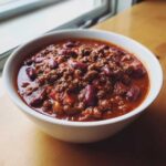 Close-up of a white bowl filled with thick, rich chili featuring ground beef and kidney beans, part of the best chili recipe.