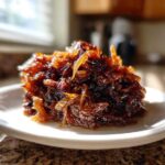 A close-up, sunlit mound of deeply browned caramelized onions served on a small white plate.