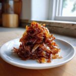 A mound of deeply browned and sticky caramelized onions served on a small white plate.