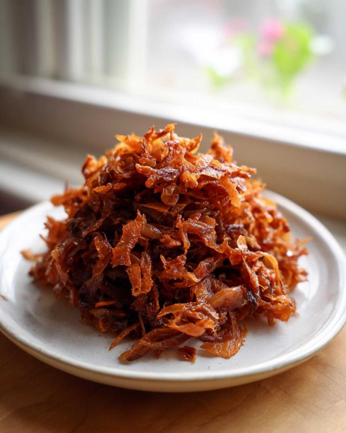 A mound of deeply browned, sticky caramelized onions piled high on a small white plate.