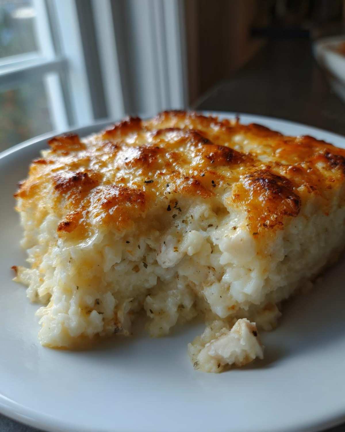 A close-up of a serving of cheesy chicken and rice casserole with a golden-brown, bubbly topping.