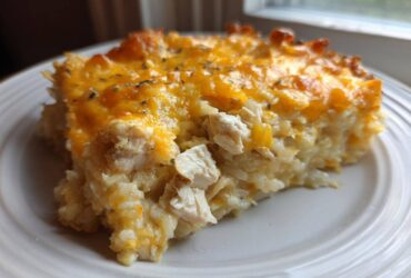 A close-up serving of cheesy chicken and rice casserole topped with melted cheddar cheese.