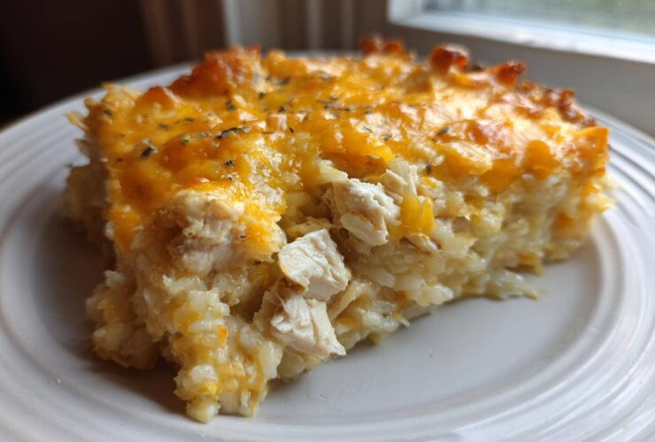 A close-up serving of cheesy chicken and rice casserole topped with melted cheddar cheese.