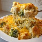 A spoonful of cheesy chicken broccoli rice casserole being lifted, showing long, melted cheese strings.