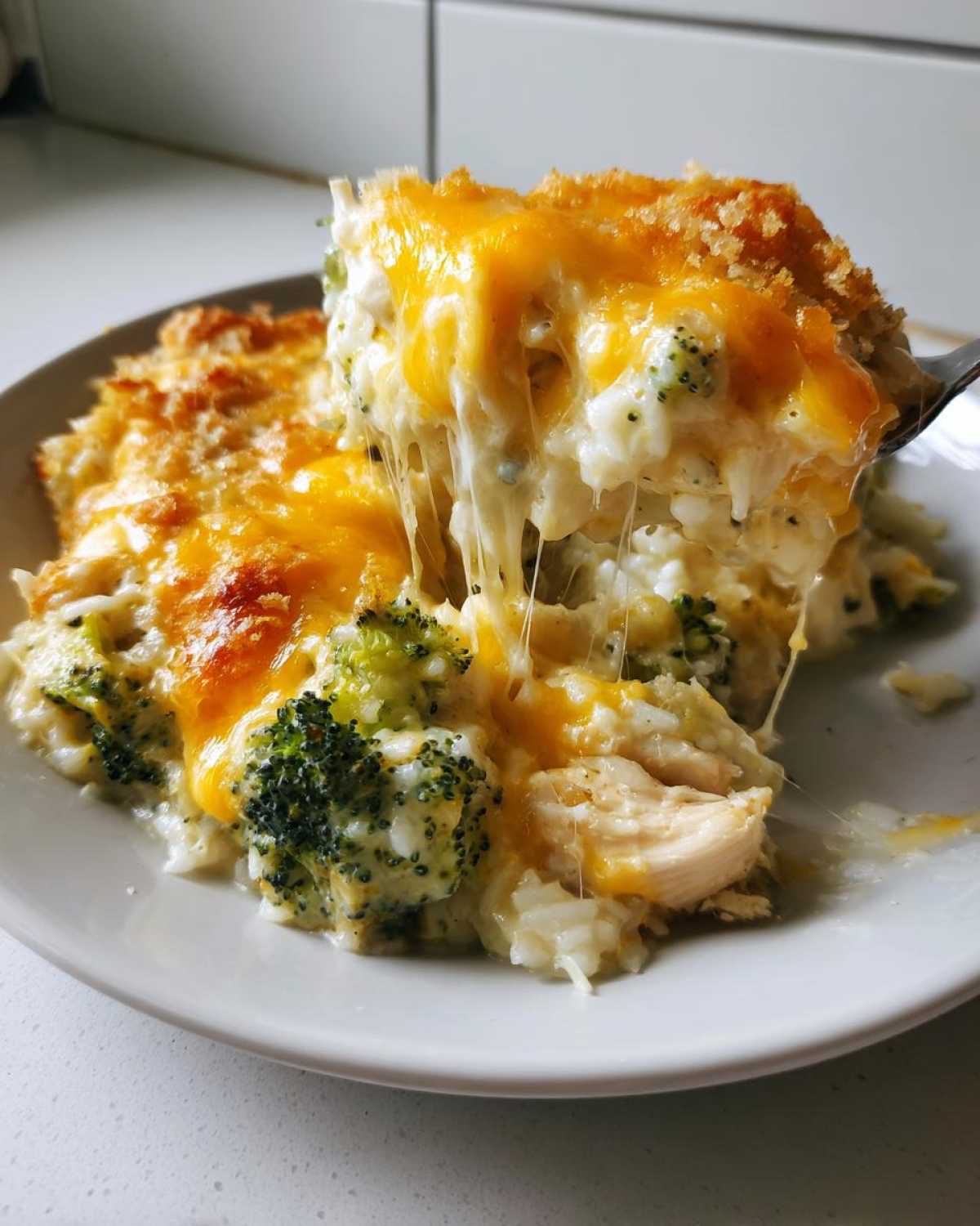 A fork lifts a cheesy, gooey serving of chicken broccoli rice casserole topped with melted cheddar.