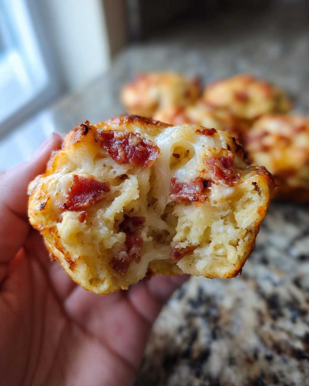 A hand holding a torn-open pizza muffin showing gooey cheese and pepperoni inside, highlighting the texture of the pizza muffins.