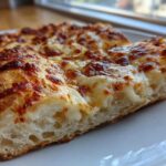 Close-up of a thick slice of cheesy pizza showing the airy crumb structure of the sourdough discard pizza dough.