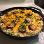 Close-up of cheesy sausage and rice casserole topped with melted cheddar and fresh parsley in a black skillet.