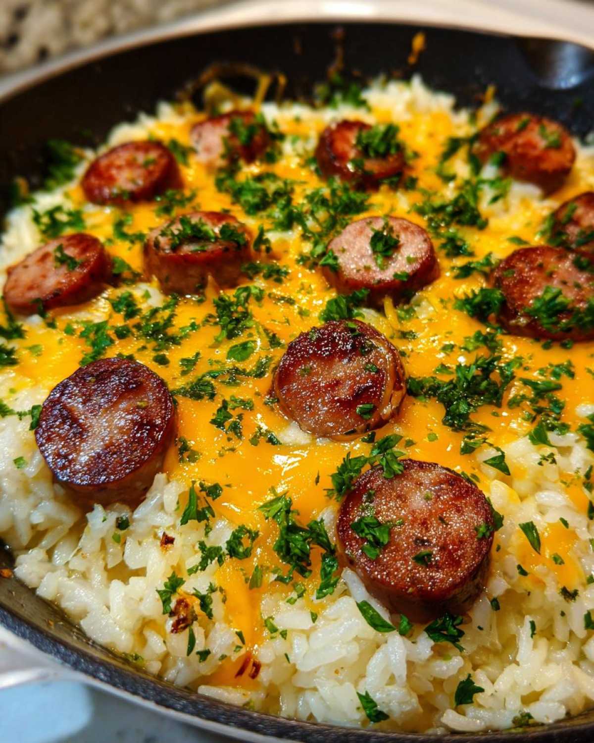 Close-up of cheesy sausage and rice topped with melted cheddar and fresh parsley in a black skillet.
