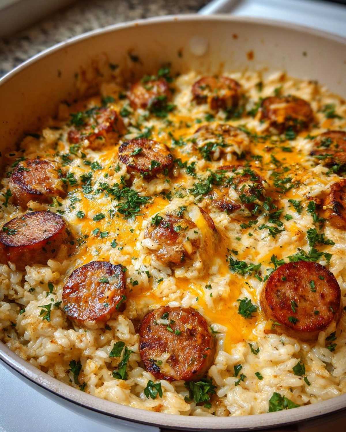 Close-up of cheesy sausage and rice dish topped with melted cheddar and fresh parsley in a skillet.