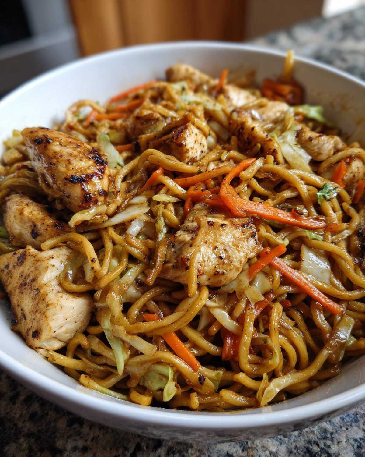 Close-up of a bowl filled with homemade chicken chow mein recipe, featuring noodles, grilled chicken pieces, and shredded carrots and cabbage.